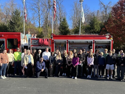 Students and community officials pose for a photo by a firetruck.